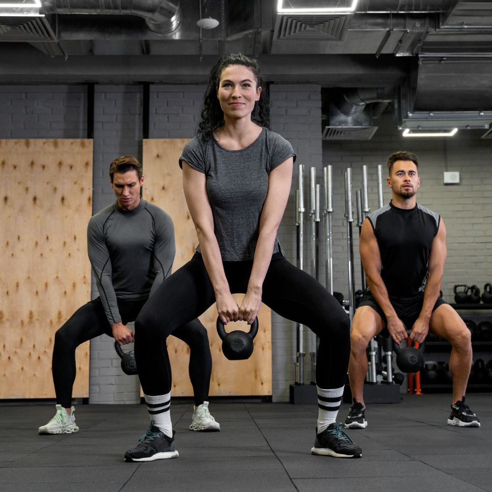 Three athletes performing kettlebell squats together in modern gym